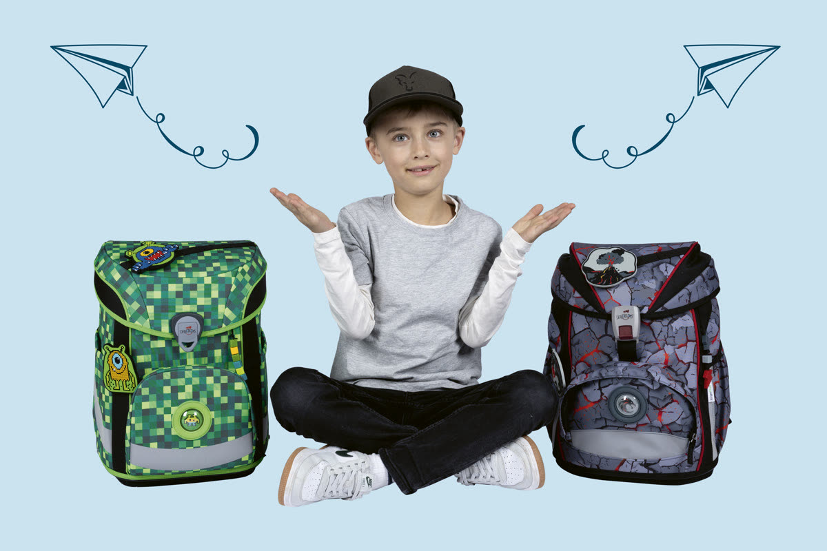 Ein Junge mit Kappe sitzt zwischen zwei DerDieDas Schulranzen und zuckt fröhlich mit den Schultern
