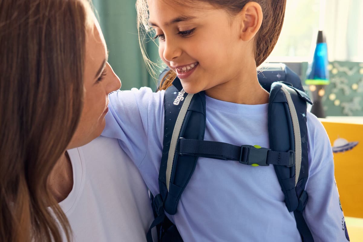 Mädchen trägt einen Ergobag Schulranzen mit geschlossenem Brustgurt, die Mutter schaut lächelnd zu