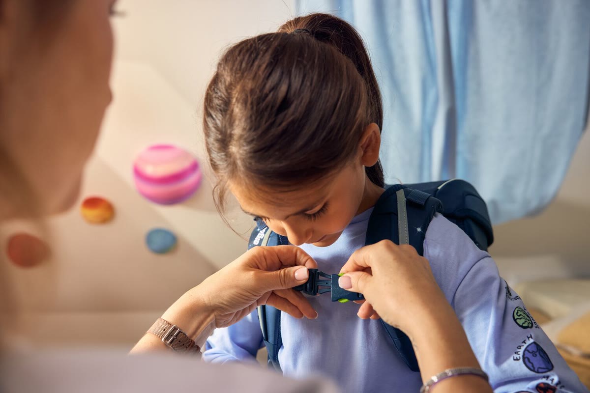 Eine Erwachsene schließt den Brustgurt eines Ergobag Schulranzens am Mädchen