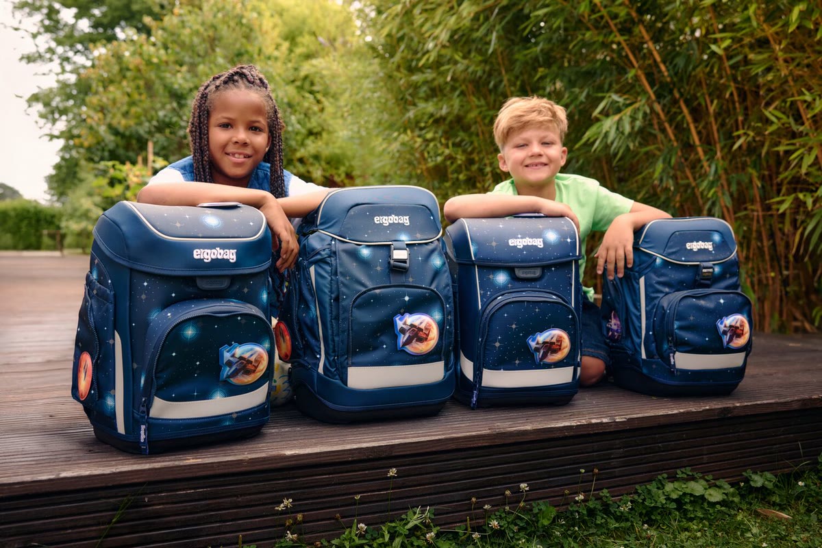 Zwei Kinder lehnen sich auf vier dunkelblaue Ergobag Schulranzen auf einer Holzterrasse