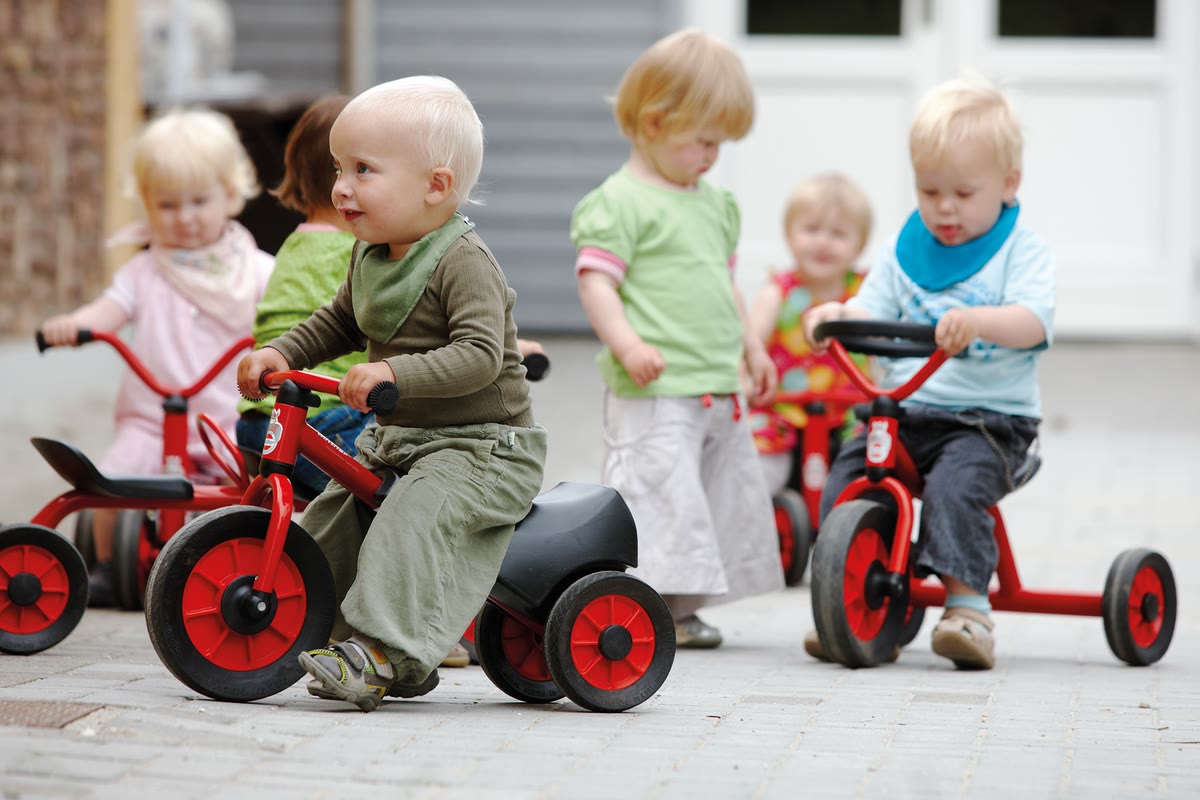 Krippenkinder fahren auf kleinen roten Winther-Dreirädern
