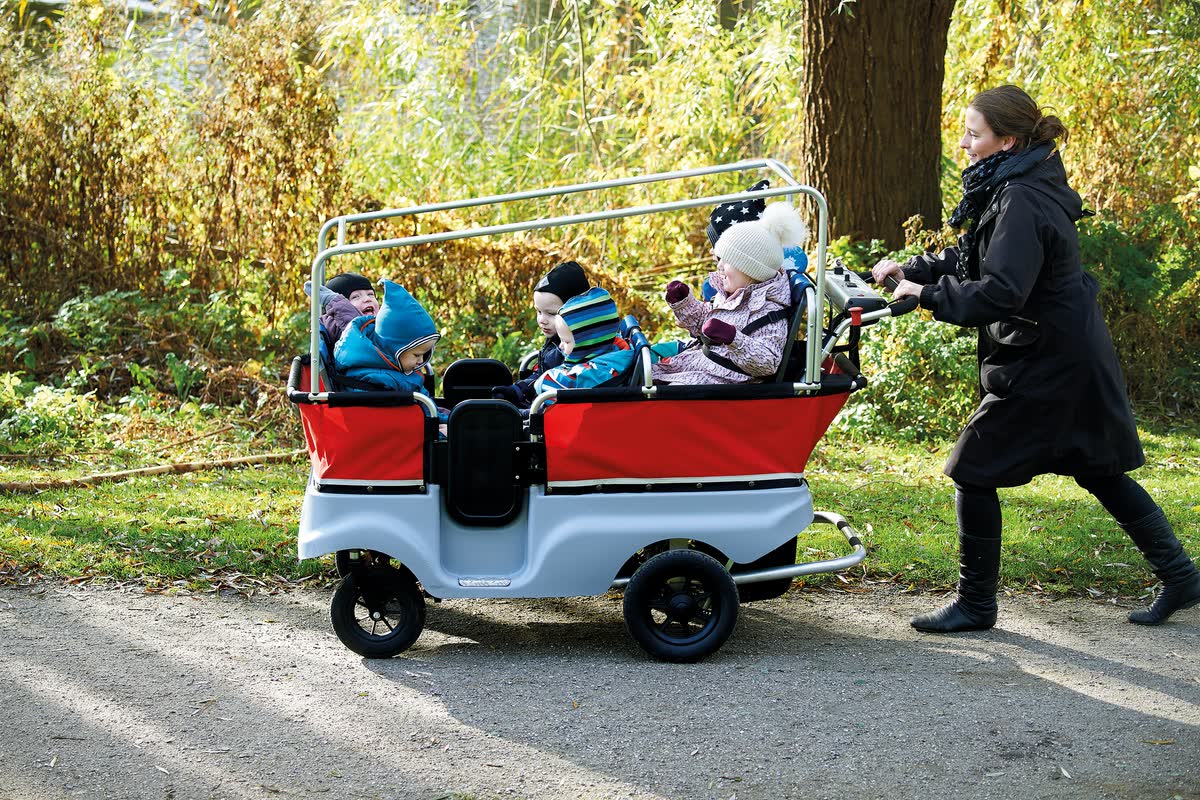 Erzieherin schiebt einen voll besetzten Winther E-Turtle Kinderbus einen Weg entlang