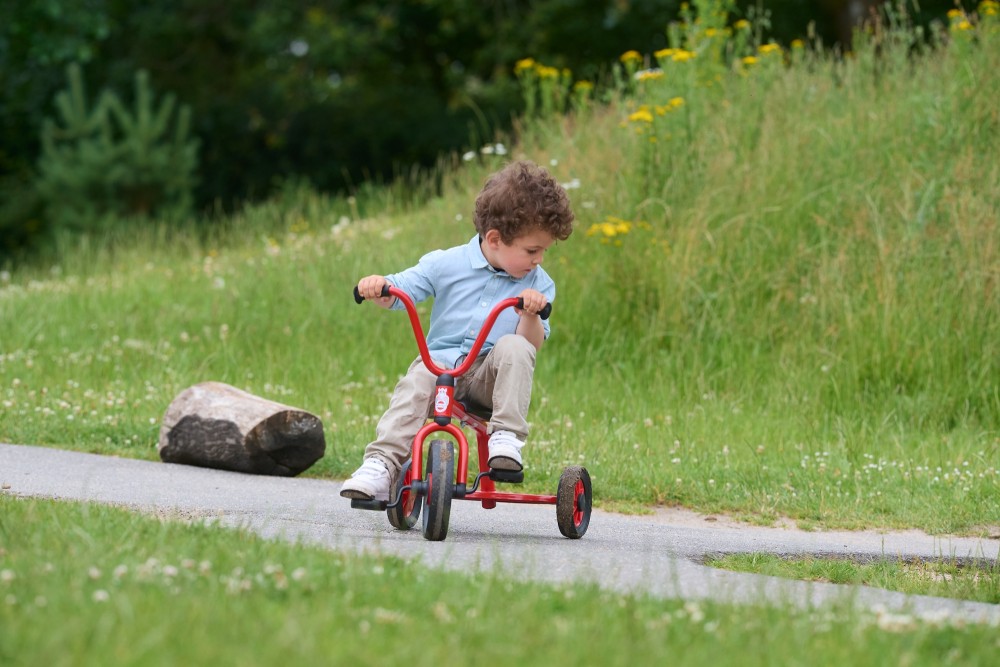 Kleinkind fährt mit dem Winther Mini Viking Krippen Dreirad mit Steg einen Weg entlang