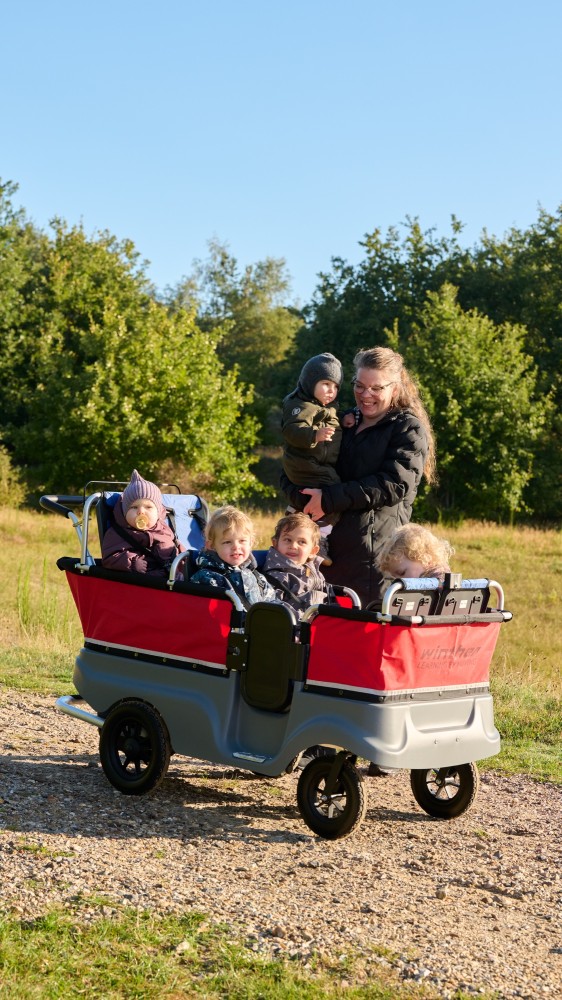 Erzieherin schiebt den Winther Turtle Kinderbus für 6 Kinder mit Kindern einen Waldweg entlang