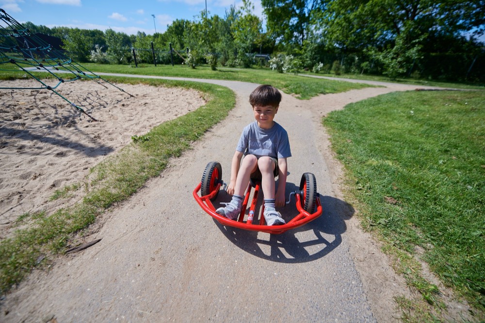 Junge fährt mit dem Winther Viking Swingcart klein einen Spielplatzweg entlang